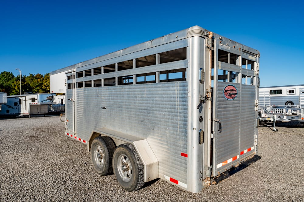 Silver aluminum two-axle horse trailer on a gravel lot with a clear blue sky.