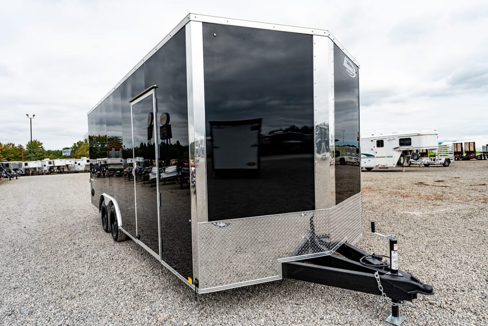 Black enclosed cargo trailer with diamond-plate front, hitched on a gravel lot; tandem wheels visible.