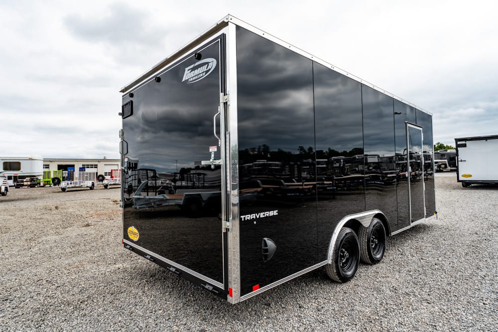 Black enclosed cargo trailer with dual axles in a gravel lot, chrome trim and rear doors visible.
