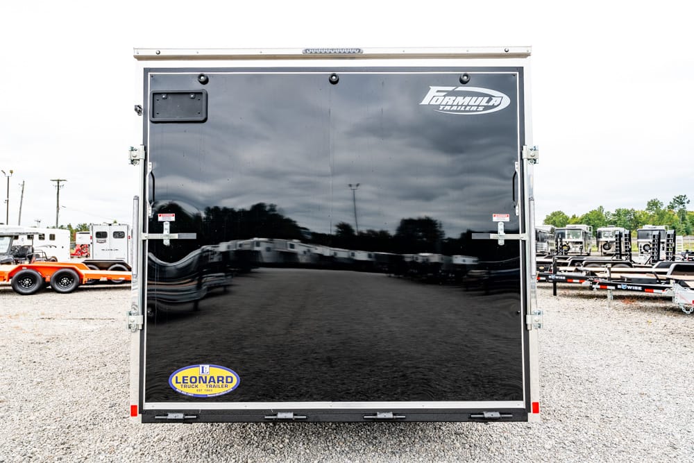 Rear of a glossy black trailer with chrome trim and Formula Trailers logo on the top-right, Leonard sticker at bottom-left on a gravel lot.