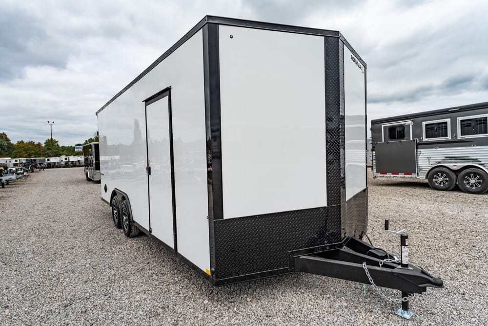 White enclosed cargo trailer with black diamond-plate front, dual axles, and a hitch in a gravel lot at a trailer yard.