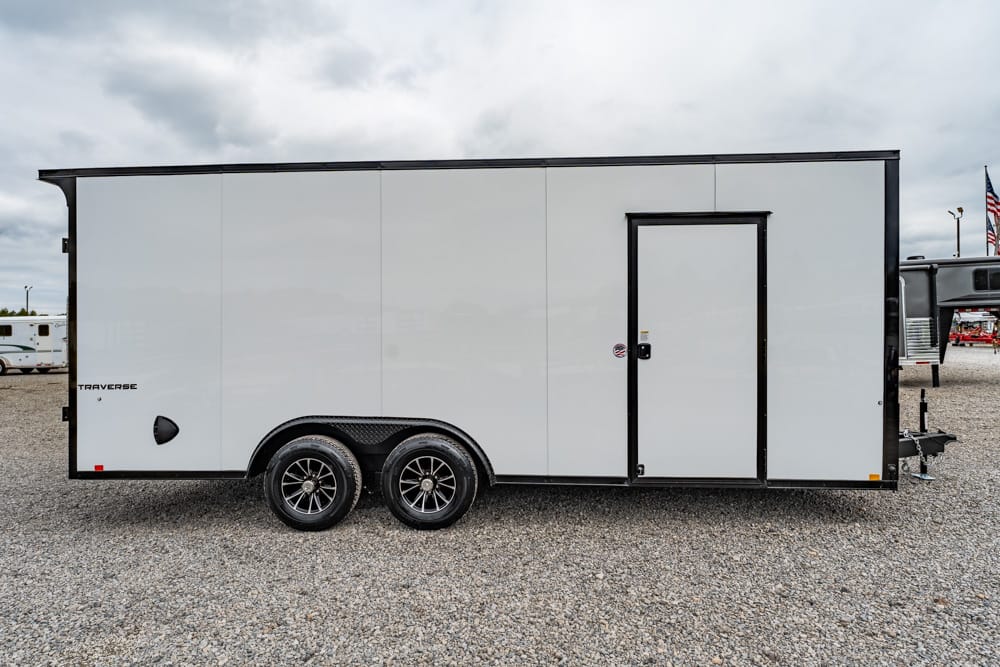 White enclosed dual-axle cargo trailer with black trim parked on a gravel lot. A side door is visible near the front.