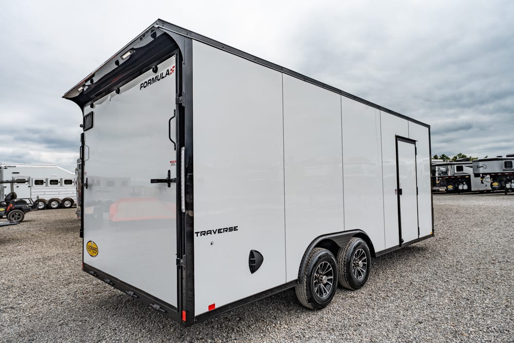 White enclosed cargo trailer with dual axles on a gravel lot.