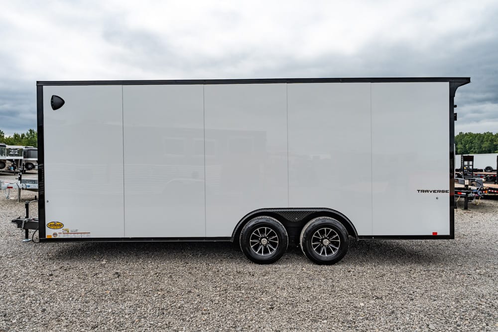 White enclosed cargo trailer with black trim and dual rear wheels parked on a gravel lot, side view.