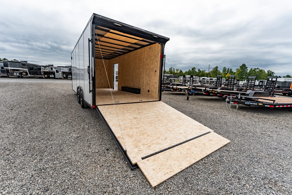 Open cargo trailer with the ramp lowered for loading on a gravel lot, surrounded by other trailers in a storage yard.