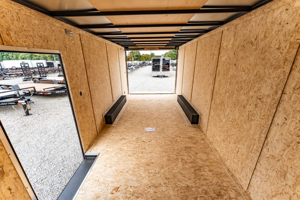 Empty plywood-walled trailer interior with benches along the sides, looking toward the open rear yard.
