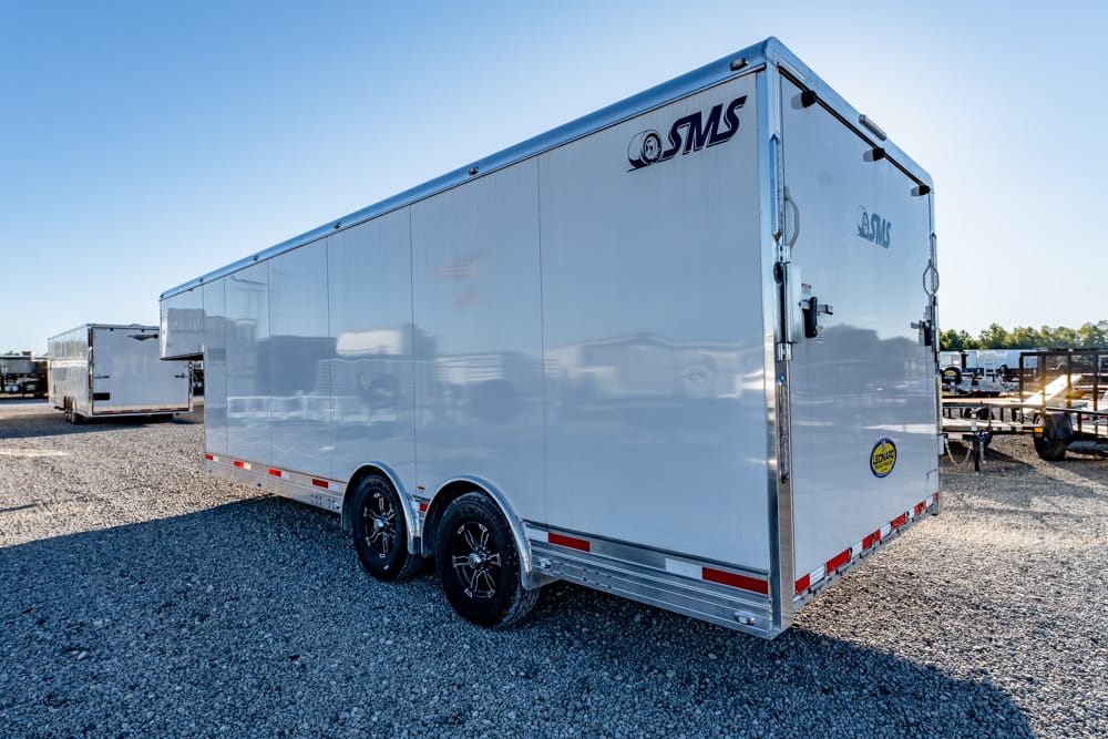 White enclosed cargo trailer with two axles and SMS logo parked on a gravel lot.