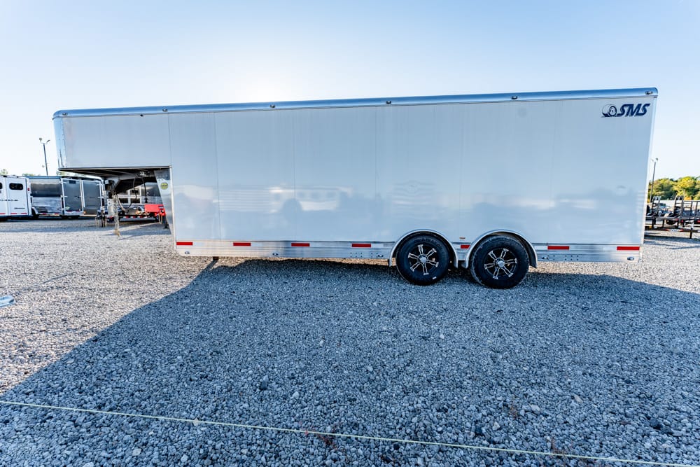 Large silver enclosed cargo trailer with two axles parked on a gravel lot.