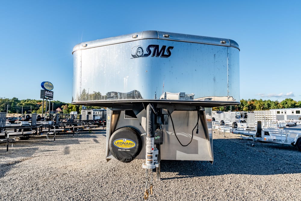 Shiny silver trailer in a gravel lot reflecting nearby buildings and blue sky.