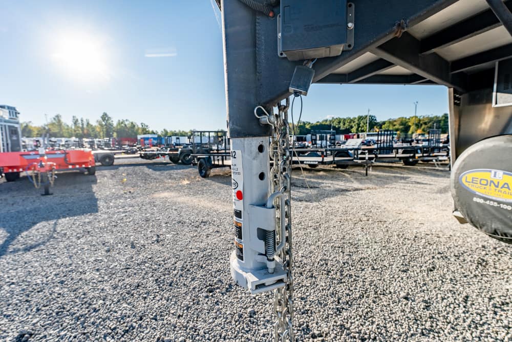 Close-up of a trailer hitch jack with safety chains, on a gravel lot with trailers in the background.