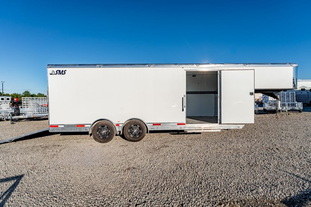 White cargo trailer with an open side door on a gravel lot under a clear blue sky.