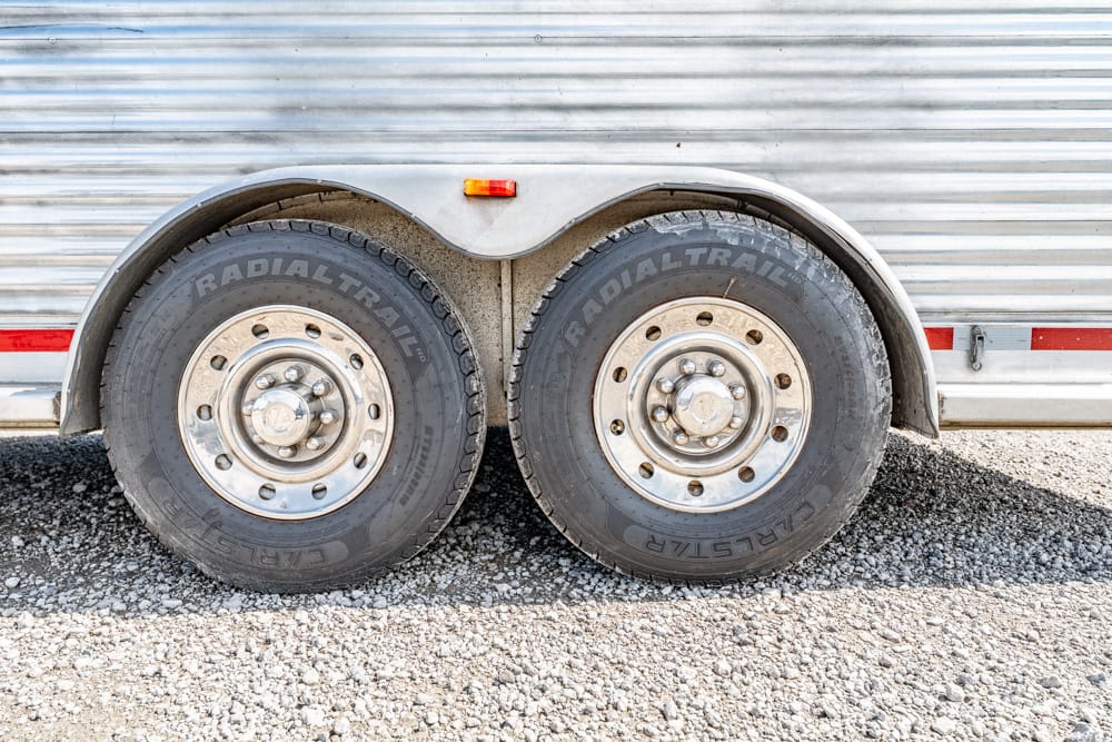 Dual-axle trailer wheels with silver rims and black radial tires under a corrugated metal trailer.