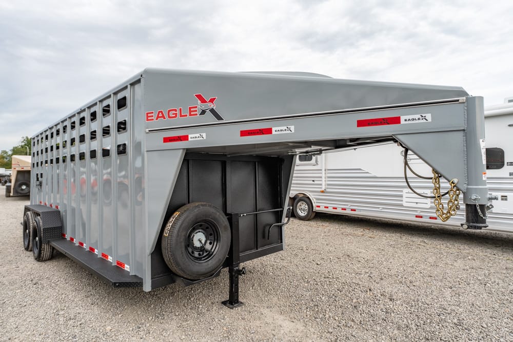 Grey Eagle-brand gooseneck livestock trailer parked on gravel, showing spare tire and front tongue assembly with chain and hitch components