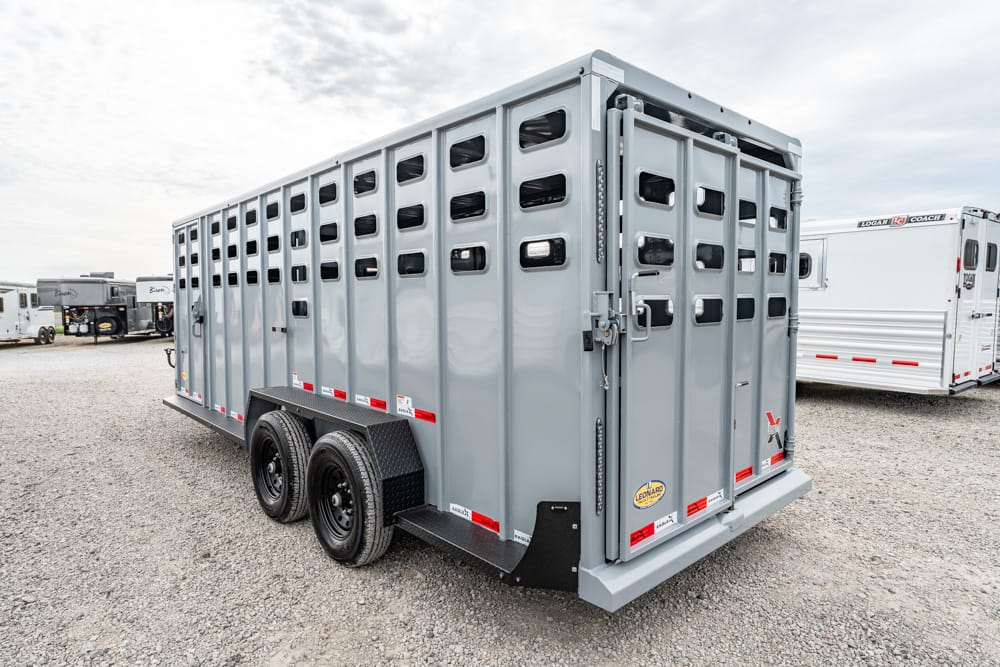 Gray two-axle livestock trailer on a gravel lot with ventilation slots along the sides and closed rear doors at the back.
