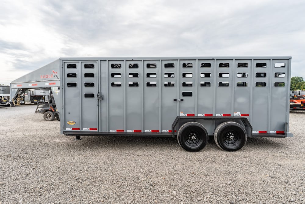 Long gray livestock trailer with side vents and dual axles on a gravel lot, other trailers visible in the background