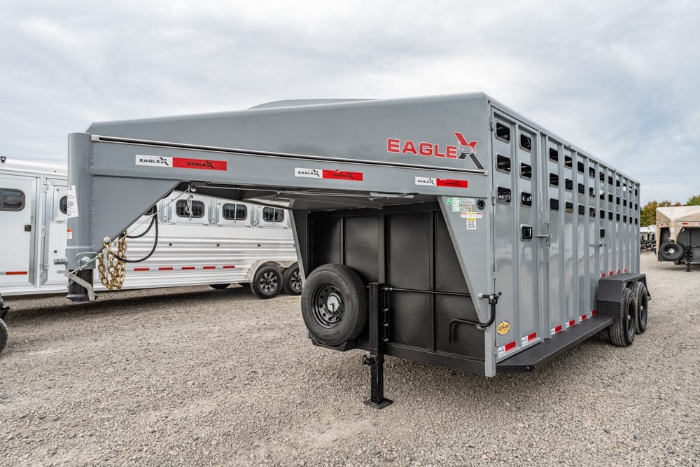 Grey Eagle gooseneck livestock trailer with vented sides and spare tire mounted, parked on a gravel lot by other trailers