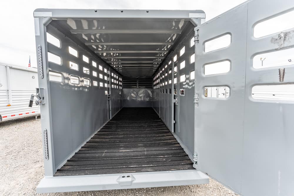 Open livestock trailer interior with metal walls, wooden floor, and side window slots for ventilation.