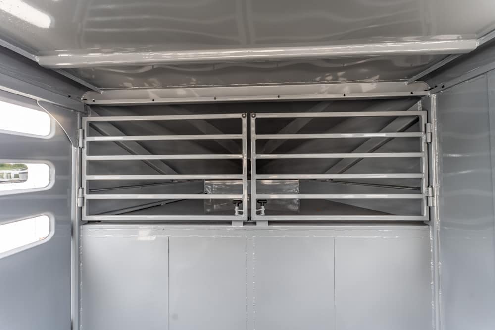 Interior of a gray livestock trailer with two metal divider gates, ventilated bars, and empty stalls.