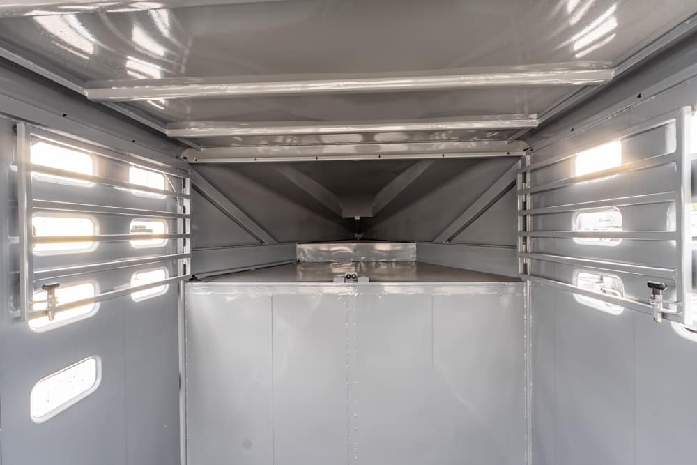 Interior of an empty gray metal trailer with ribbed side walls, small windows, and a raised loading platform at the far end.