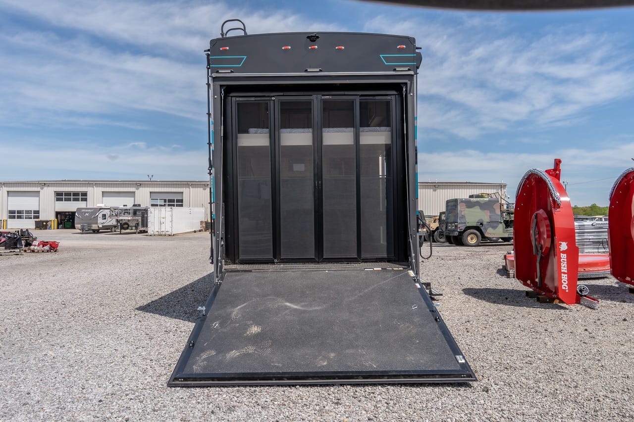 Back of a large black trailer with its ramp lowered, ready for loading in a gravel lot.