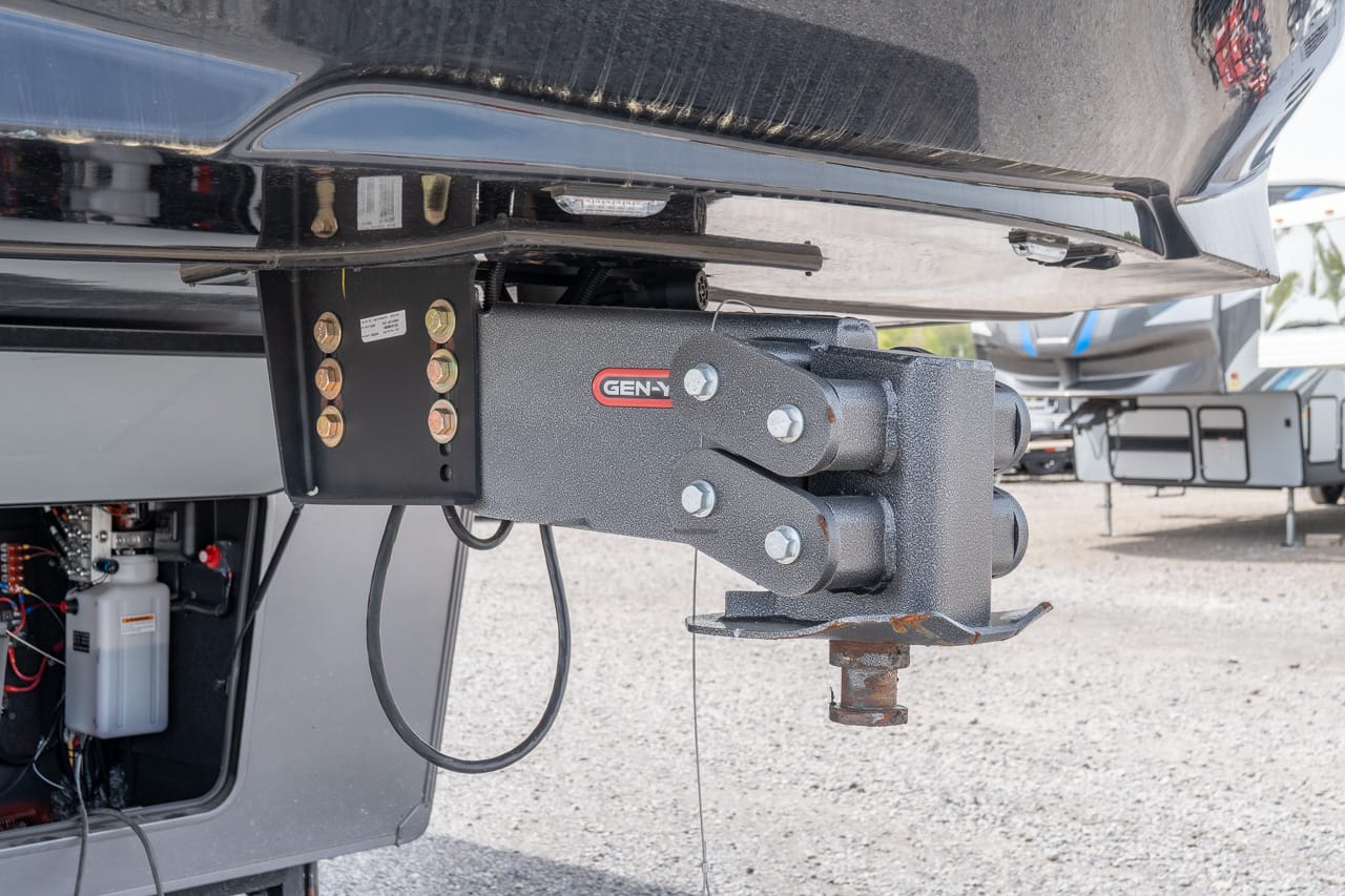 Gen-Y trailer hitch assembly mounted under a vehicle, with bolts, wiring, and a rusted hitch ball on gravel ground.