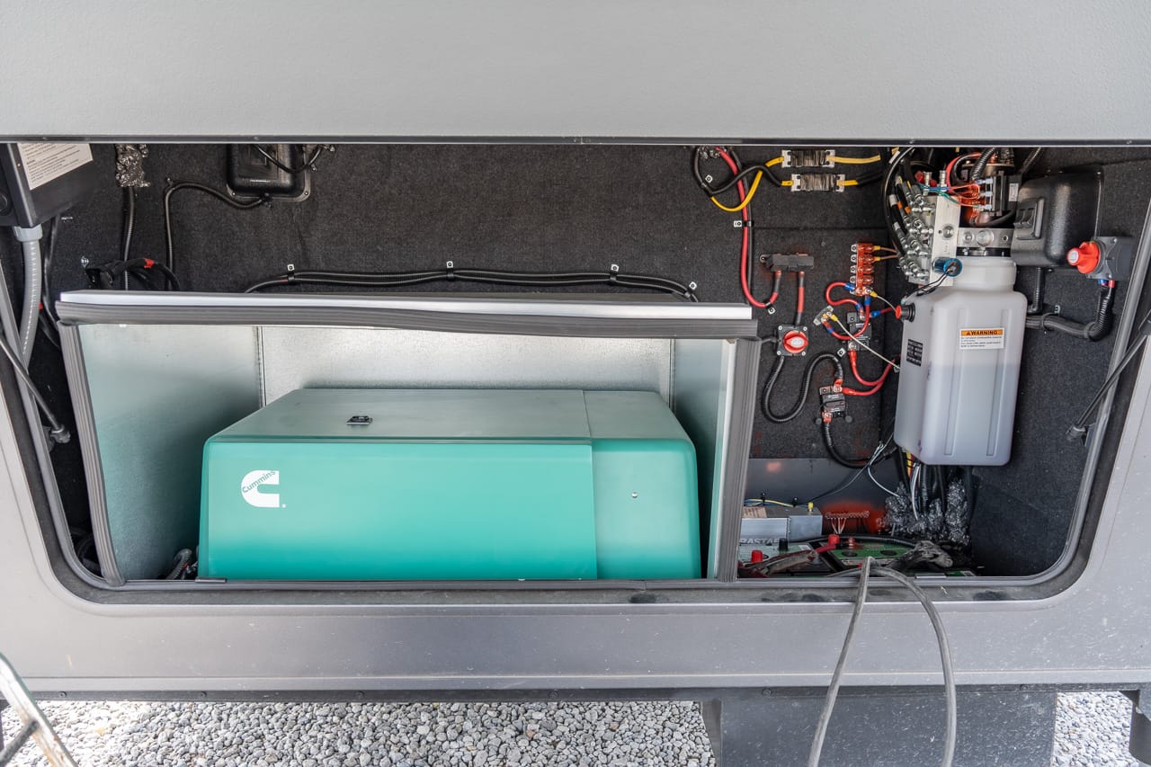 Open compartment with a teal Cummins generator, wiring, and a white reservoir on the right side.