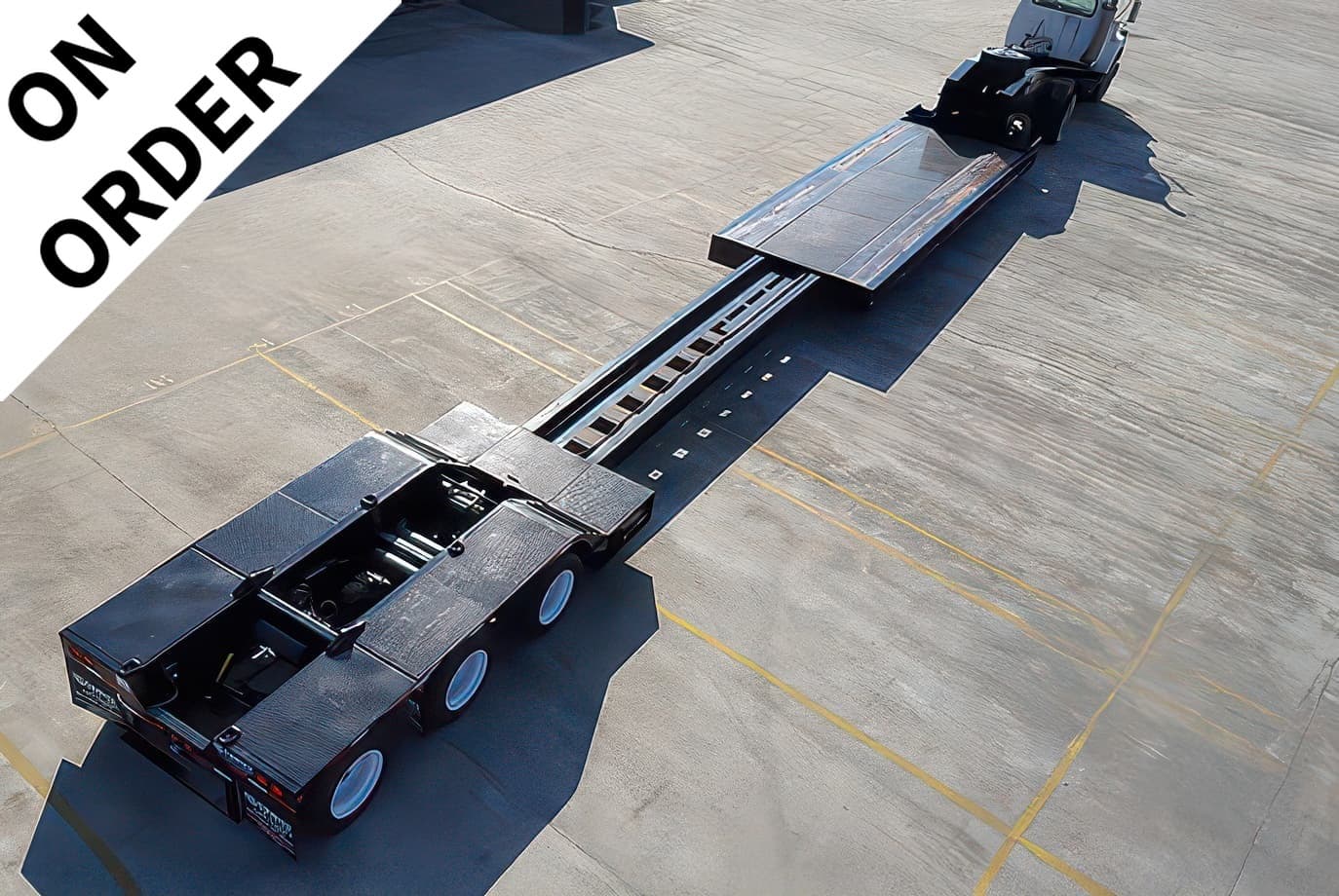 Overhead view of a long black lowboy trailer attached to a truck on a concrete tarmac, with a diagonal white banner reading 'ON ORDER' across the top-left corner.