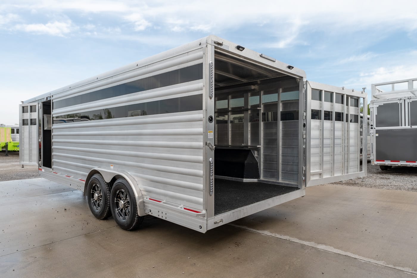 Aluminum two-axle livestock trailer with open rear ramp and visible interior stalls for loading animals.