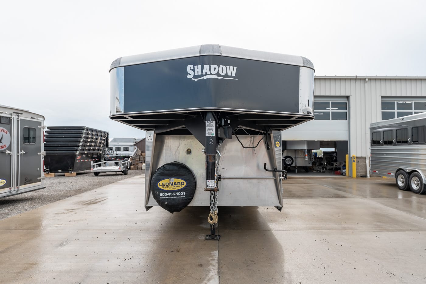 Front view of a Shadow fifth-wheel trailer on a dealership lot, with other trailers and a service bay in the background.