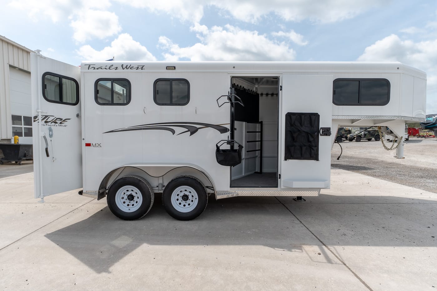 White horse trailer with living quarters, doors open to reveal the interior and mounted tack storage outside side entrance.