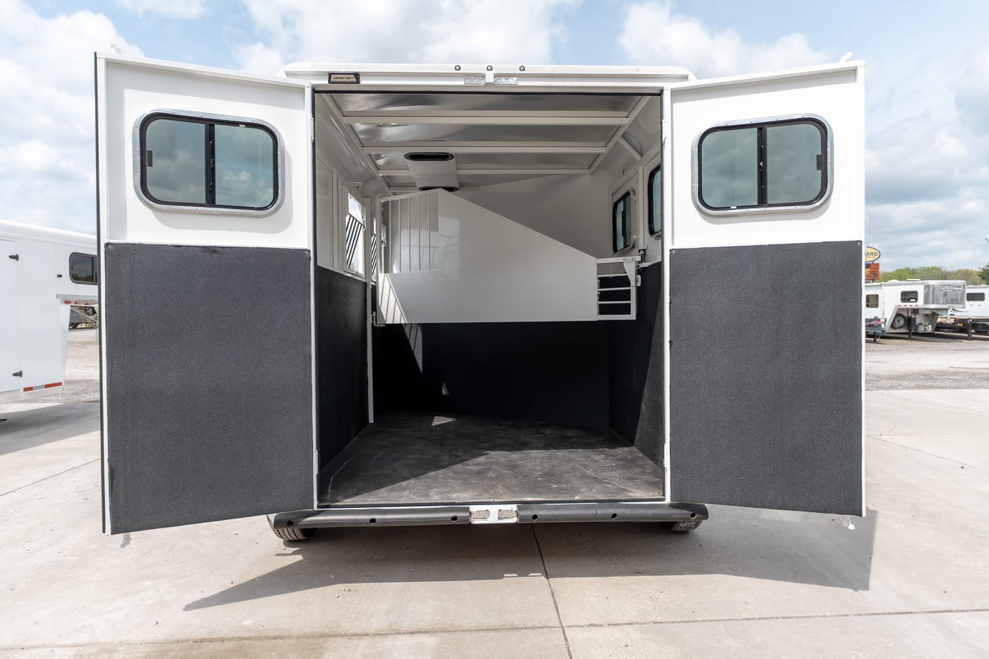 Rear view of an open white horse trailer, doors wide, revealing an empty cargo area with a divider and black wall panels