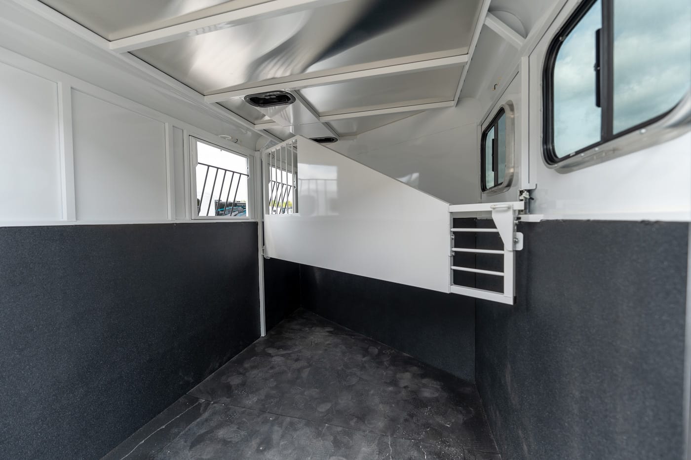 Interior of a white horse trailer with a dividing wall, rubber floor, and barred windows
