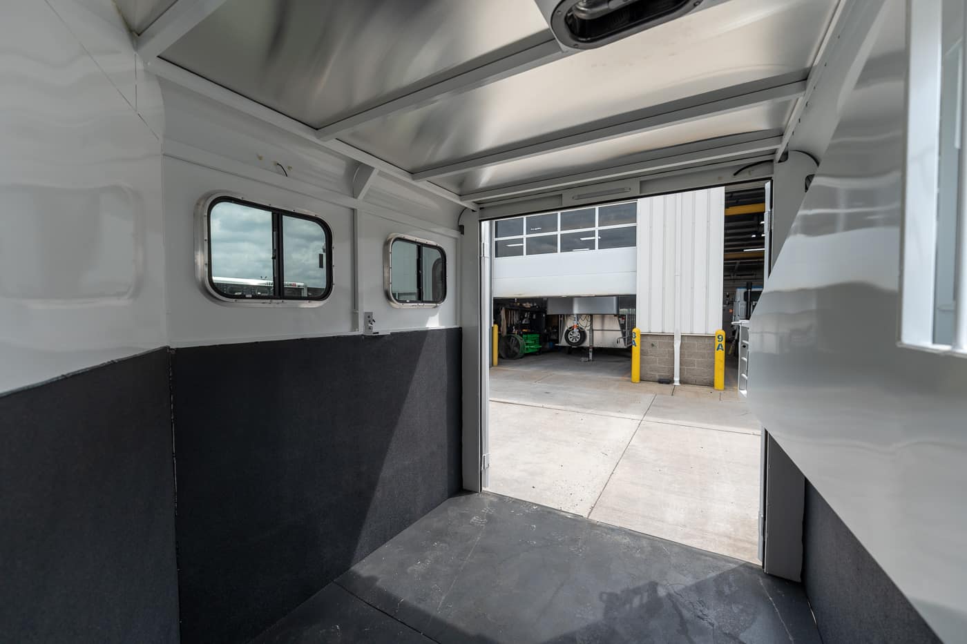 Interior of a white utility trailer with dark lower walls and an open doorway to an industrial loading area outside.