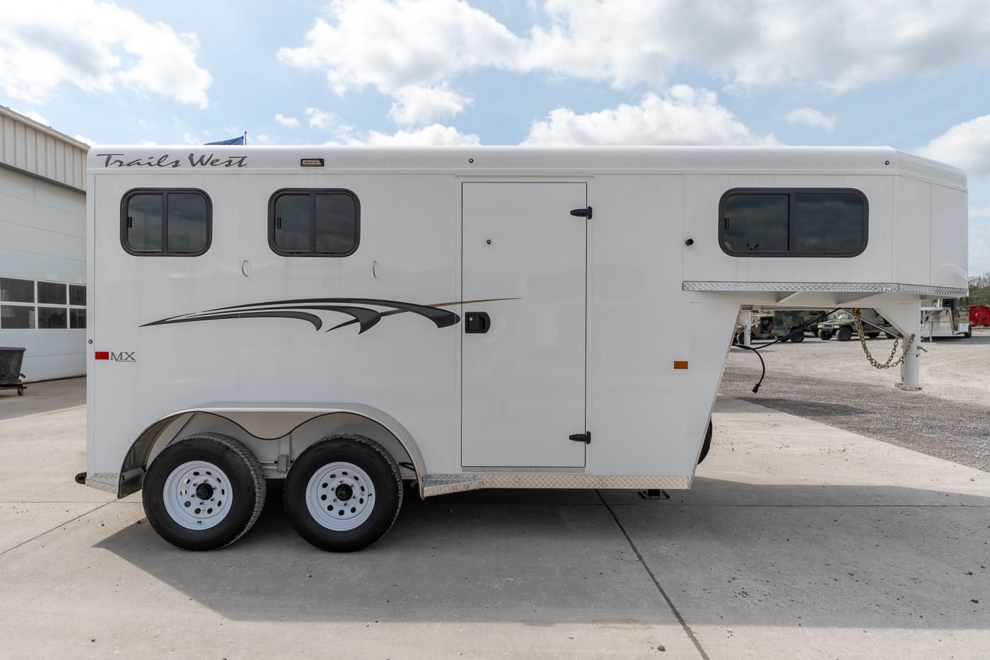 White Trails West MX horse trailer with two axles, side entry door, and black-tinted windows set on a concrete lot.
