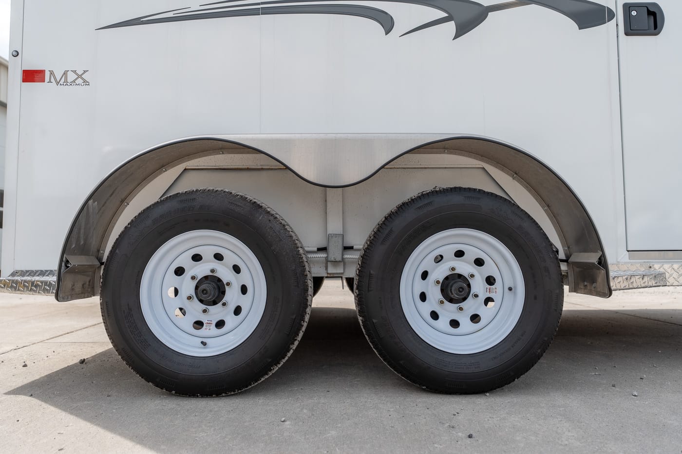 Dual-axle trailer with curved wheel wells and two white steel wheels on a paved surface