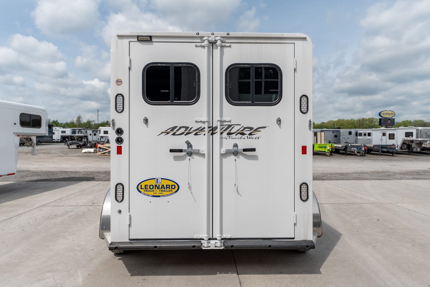 Rear view of a white horse trailer with two small windows, dual back doors, and a Leonard sticker on the bumper area.