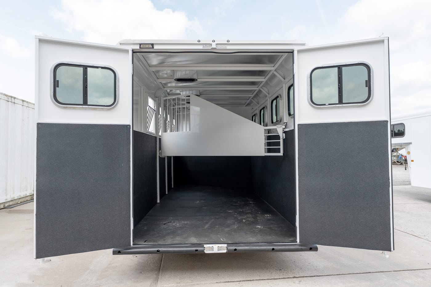 Open horse trailer interior with a raised center divider and separated stalls, rear doors wide open.