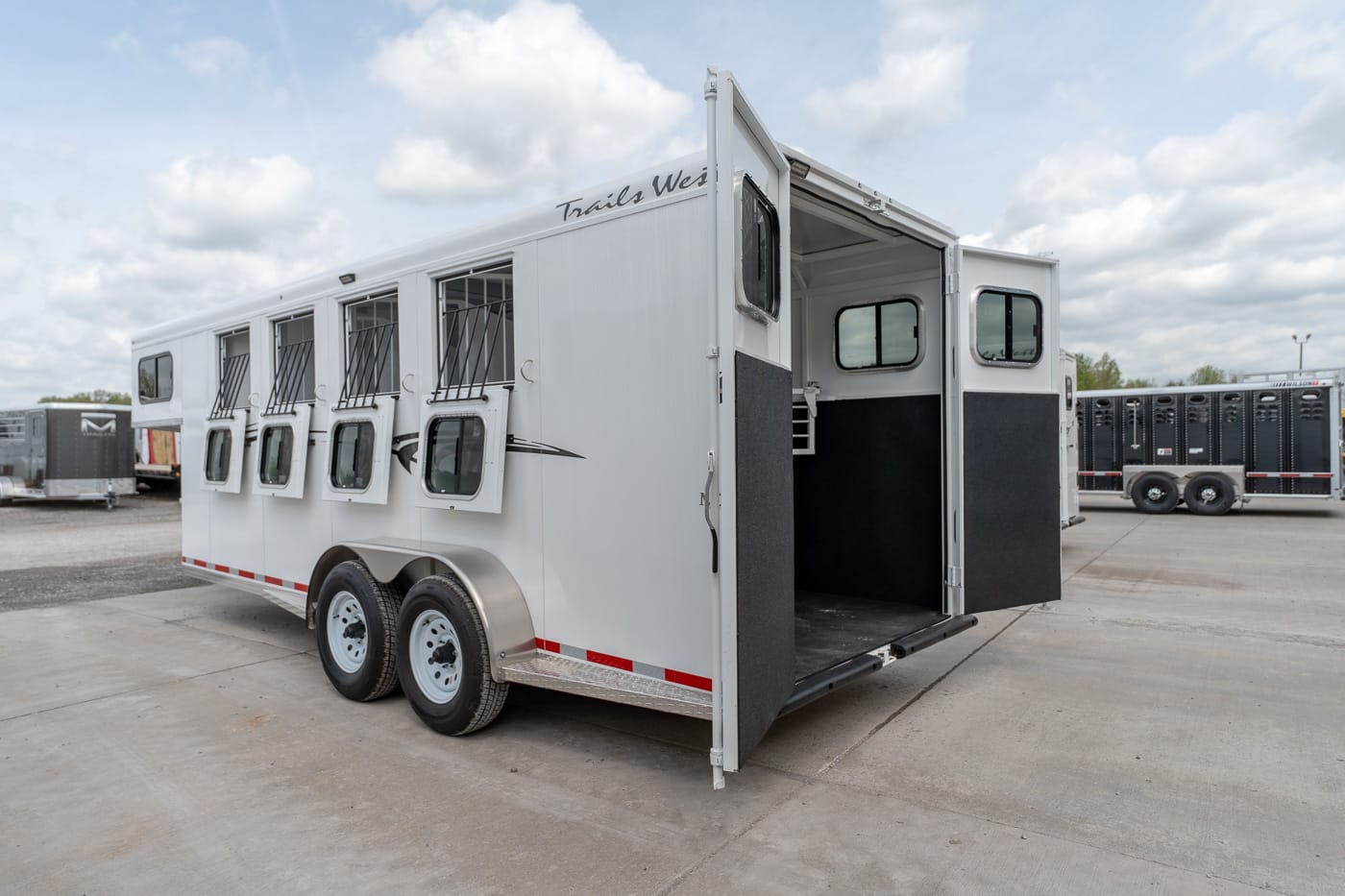 White horse trailer with multiple swing-out windows along the side and an open rear ramp.