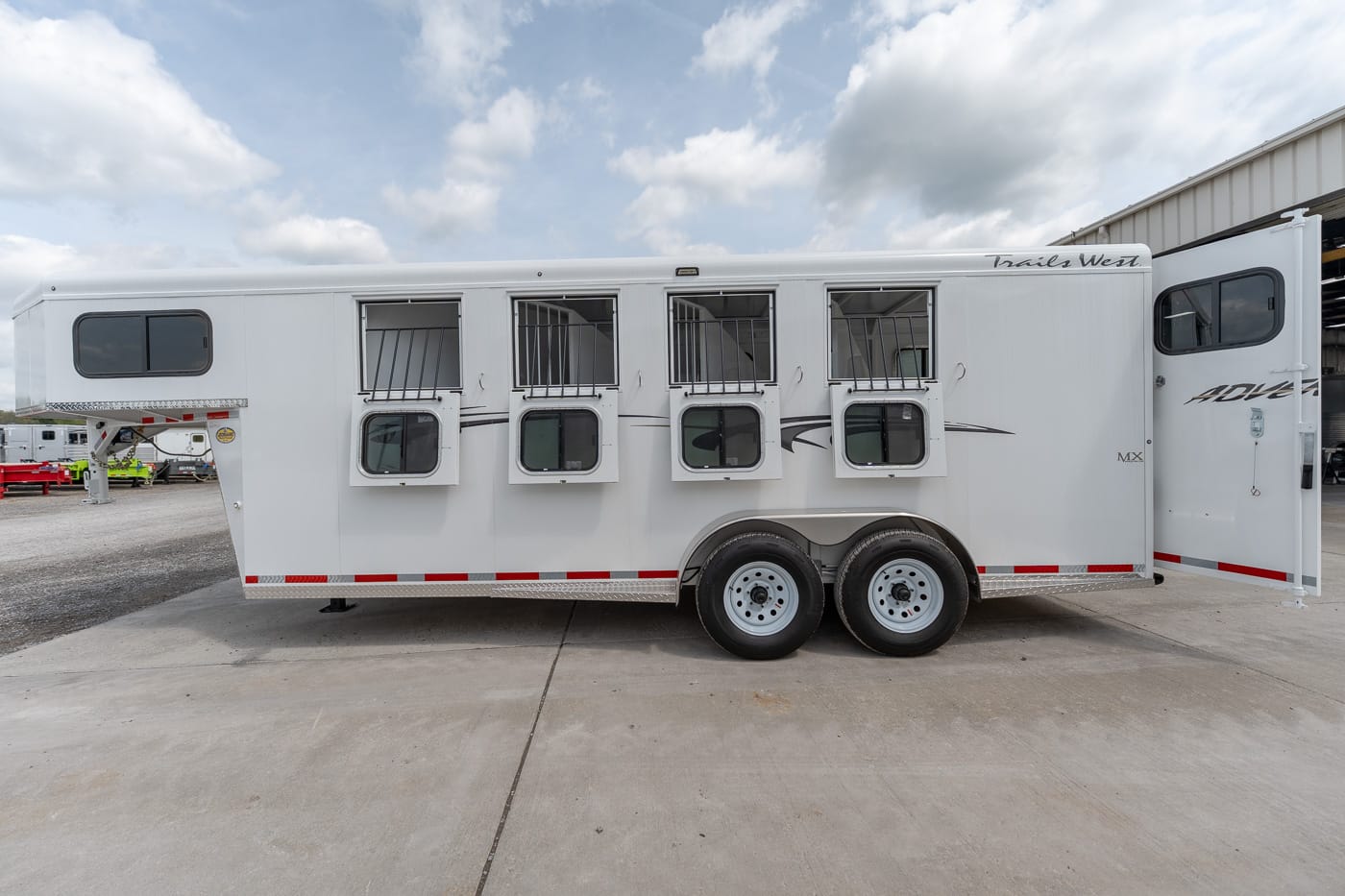White horse trailer with four horse stalls and barred windows, parked on concrete.