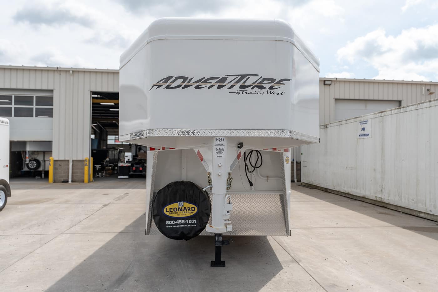 Front view of a white Adventure by Trails West gooseneck horse trailer in an industrial service yard.