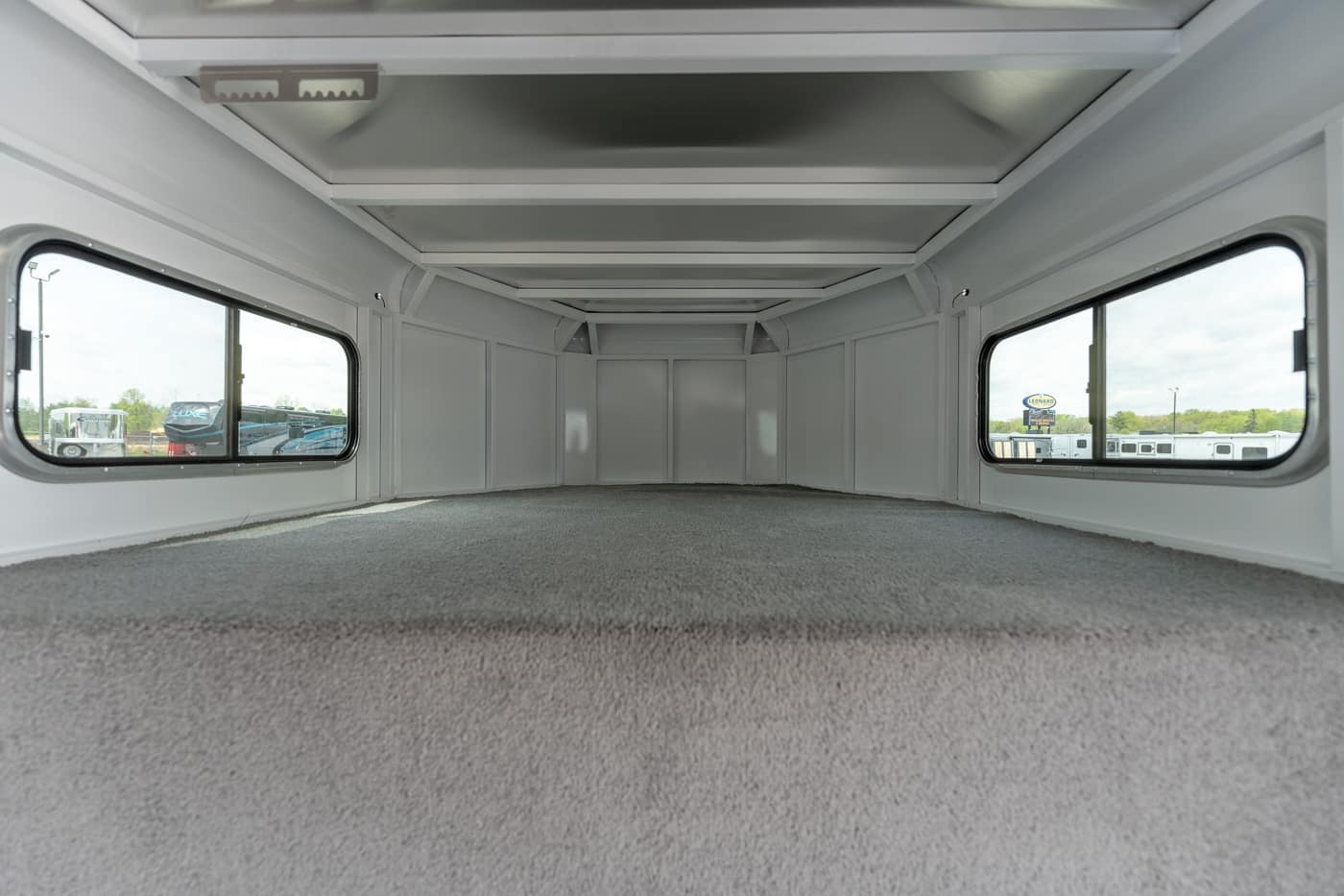 Empty trailer interior with light gray walls, carpeted floor, and large side windows for natural light.