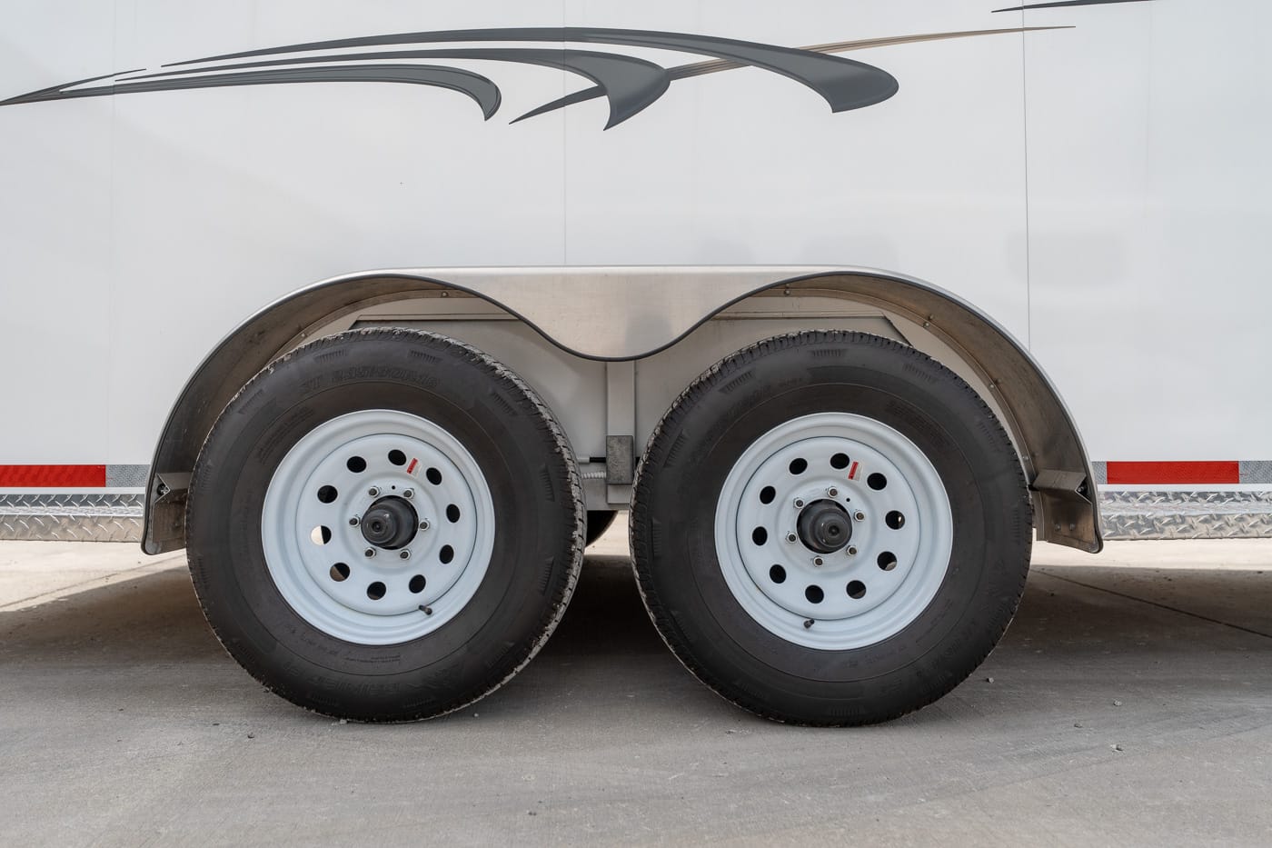 Tandem trailer wheels and fenders on a white trailer with silver rims and black tires.