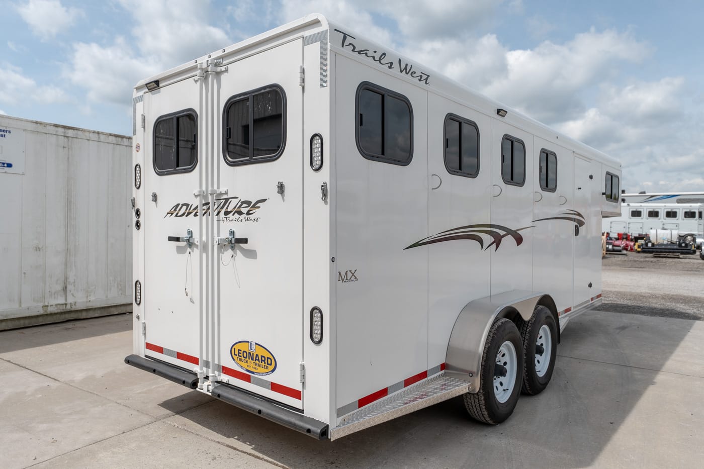 White Trail West Adventure horse trailer with two axles and multiple windows, parked in a lot under a cloudy sky.