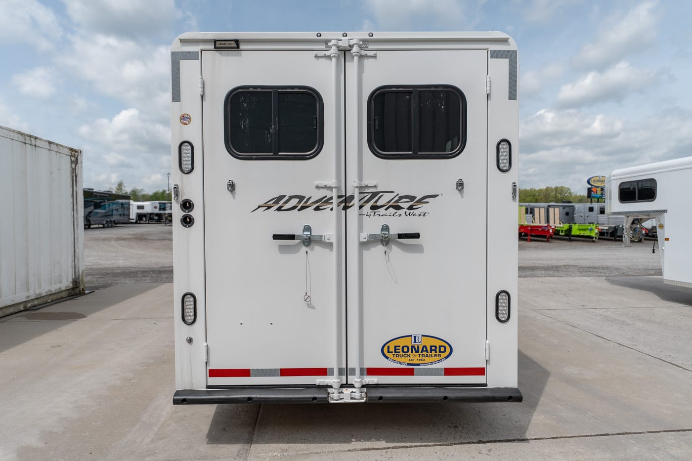 Rear view of a white horse trailer with double doors, two small windows, and a Leonard trailer logo on the lower right side.