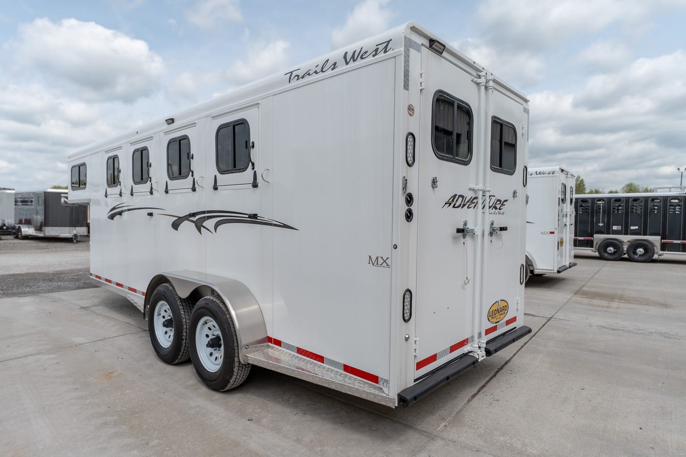 White Trails West horse trailer with two axles and multiple side windows, parked in a lot.