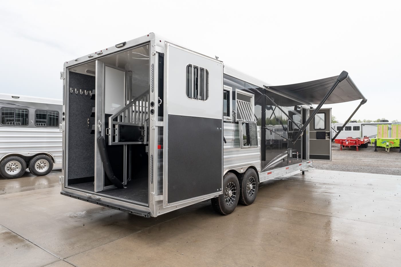 Silver horse trailer with living quarters; rear doors open, showing interior stairs and divider.