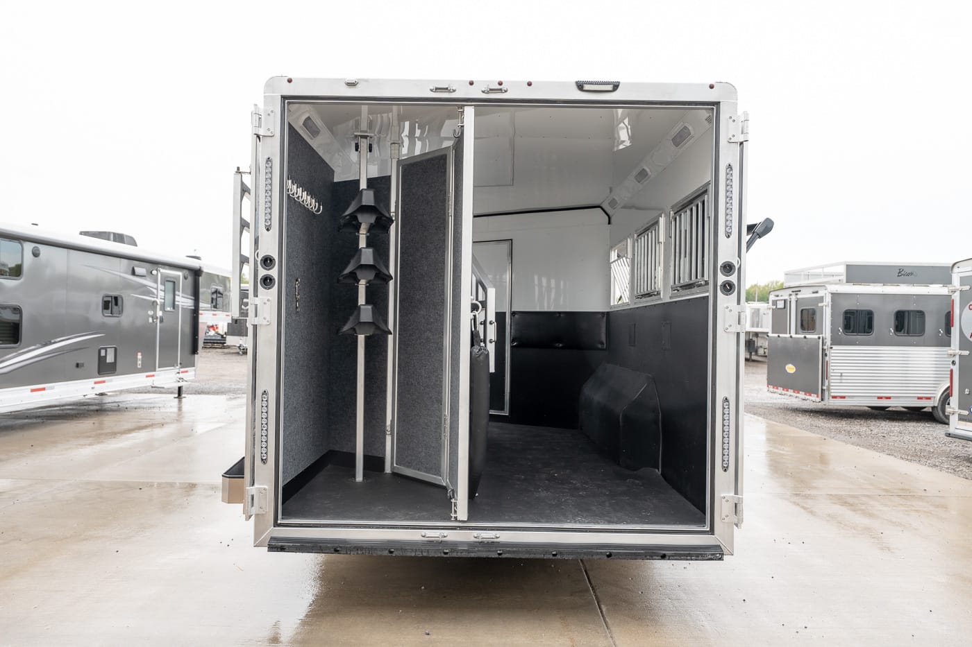 Interior of a horse trailer with a partitioned stall, saddle racks, and rubber mats at the rear door