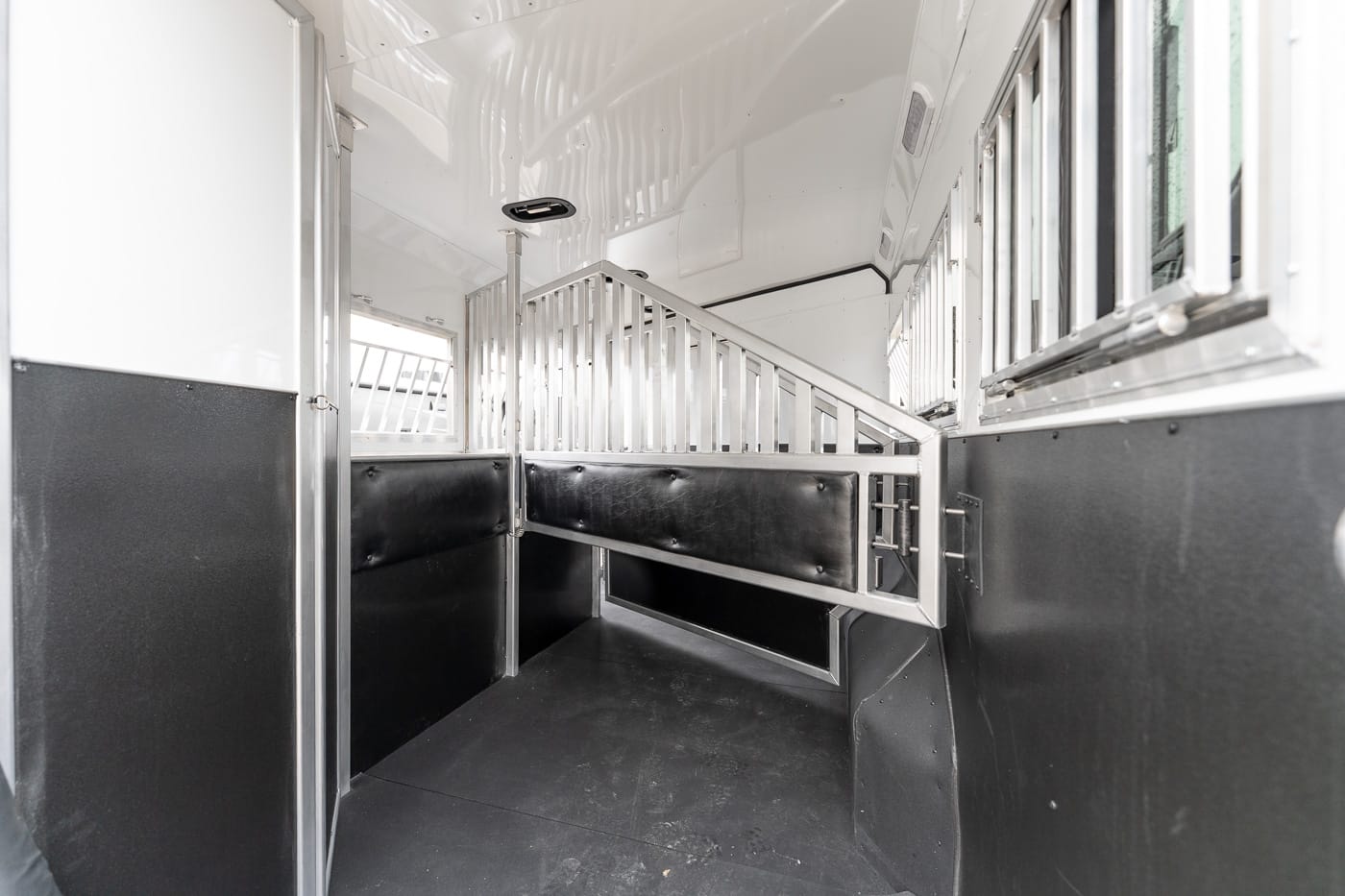 Interior of a horse trailer featuring a metal divider, padded walls, and a staircase to the upper stall area.