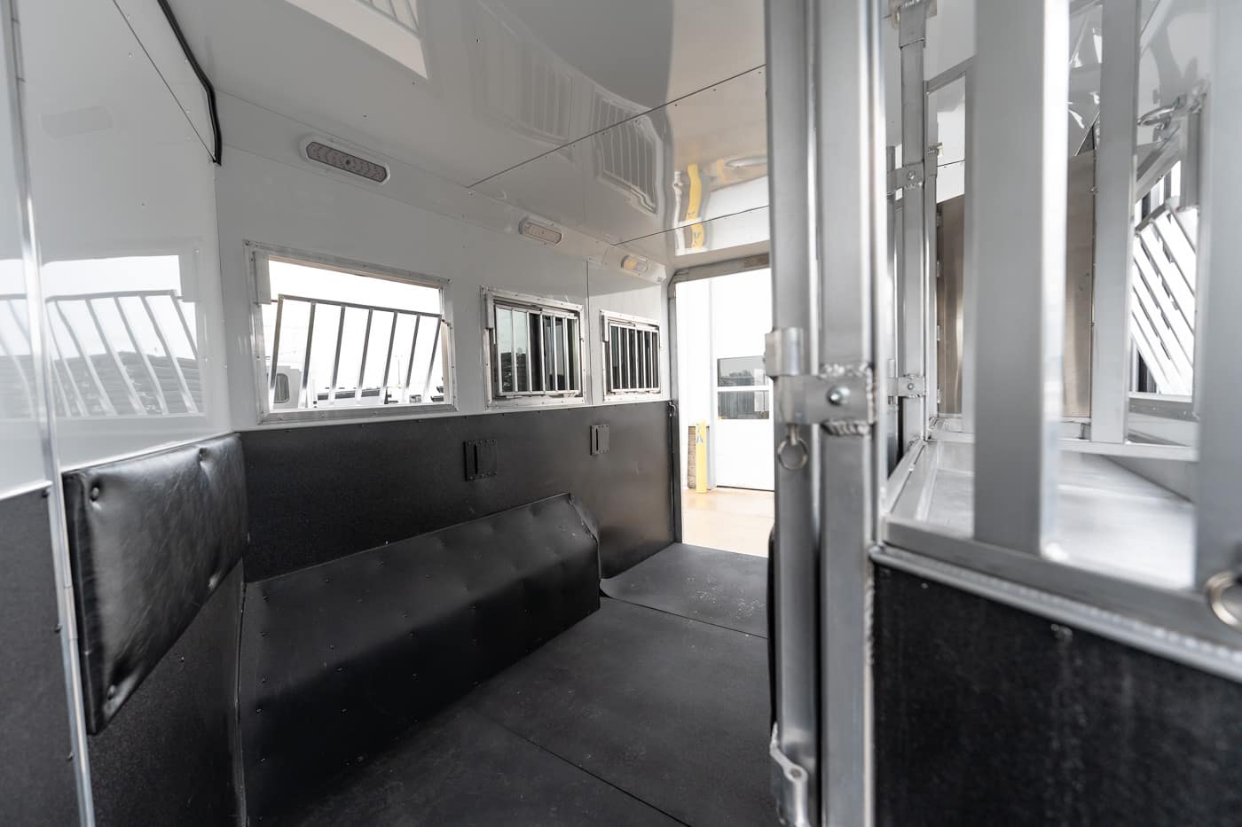 Interior of a metal livestock trailer with black padded side walls and barred windows along the side.