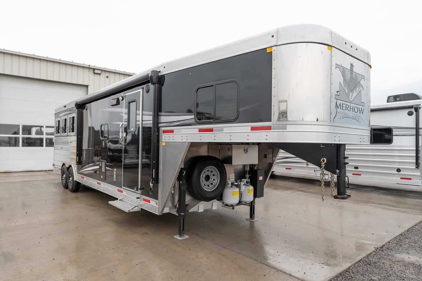 Gooseneck horse trailer with black and silver exterior parked on a concrete lot, Merhow logo visible at the front/right side edge.